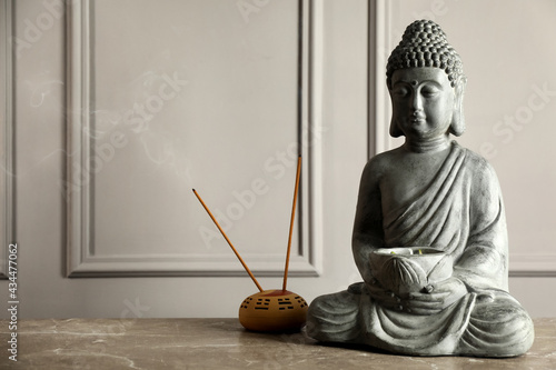 Buddha statue and incense sticks on grey table. Space for text
