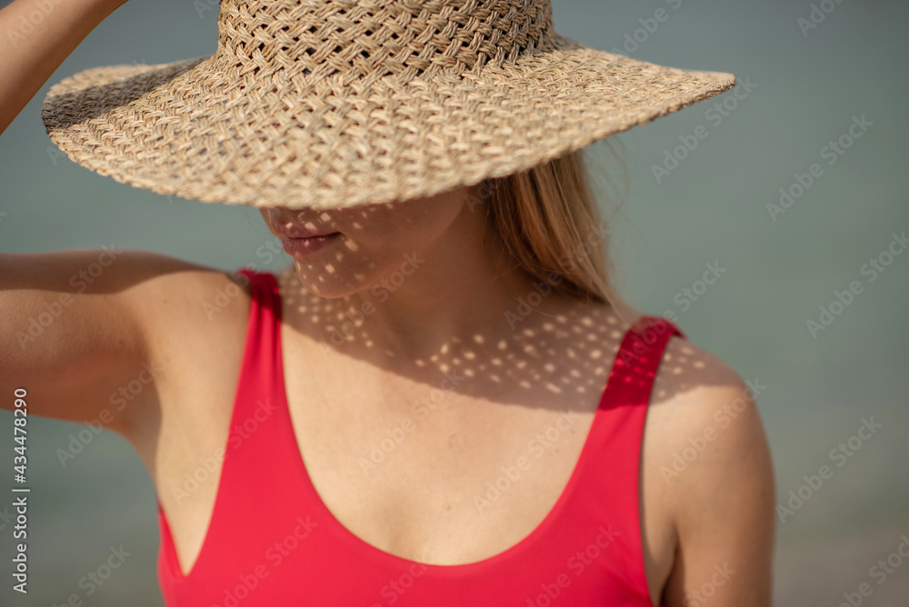 Woman with blond hair in a hat, the hat covers her face. Woman wearing red swimsuit