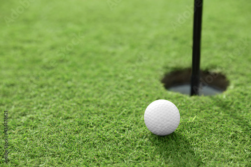 Golf ball near hole on green course, space for text