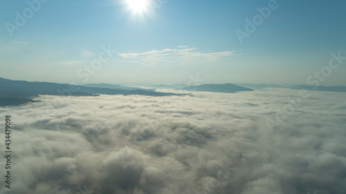 Fototapeta Naklejka Na Ścianę i Meble -  Aerial view: Mist or sea of fog cover the mountains valley. Cloudy view on top of a mount with clouds at foreground and background. ocean of clouds