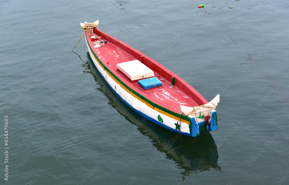 Top view of a small colorful isolated fishing boat in the lake. Ripples and reflection in the stagnant waters. 