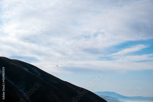 Paraglider silhouette flying on blue sky background. Nature landscape. Concept: adventure, art, travel. Blue sky background. Ushkonyr plateau, Kazakhstan. Travel in Kazakhstan concept. photo