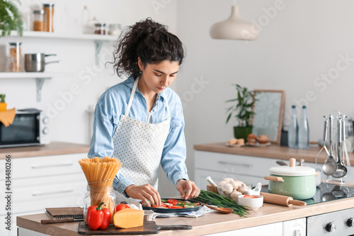 Young woman cooking tasty pizza in kitchen