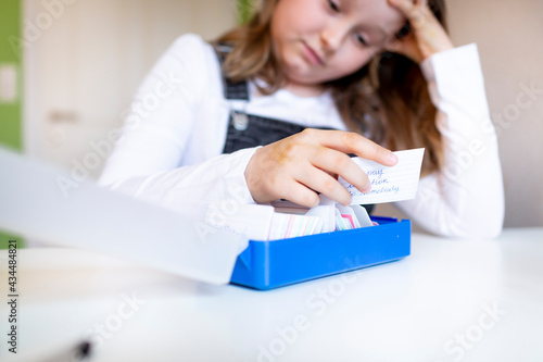 pretty young schoolgirl sitting on her desk in her room at home learning english vocabulary using flashcards during corona time