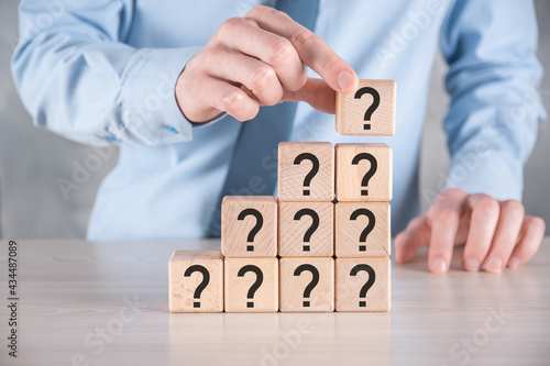 Businessman hold and put wooden cube block shape with question marks on grey table. Space for text.concept for confusion, question or solution