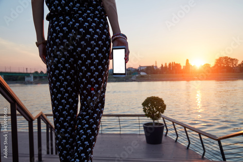 Young woman holding cellphone with blank white screen in urban city surroundings.