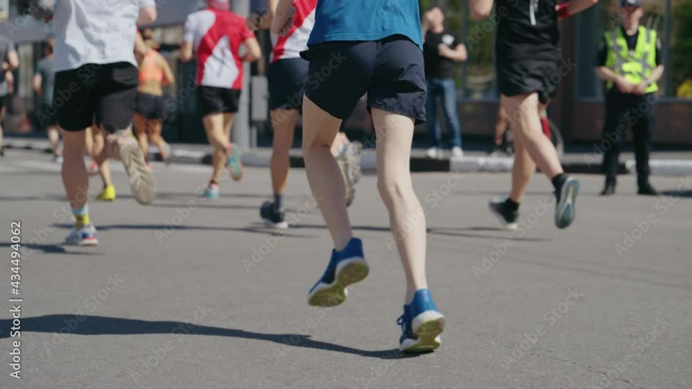Slow motion feet of athletes running marathon in city, police officer and onlookers on roadside. Partial view from behind of contestants of sports event. Healthy lifestyle. Concept of sport Slow motion feet of athletes running marathon in city, police officer and onlookers on roadside. Partial view from behind of contestants of sports event. Healthy lifestyle. Concept of sport