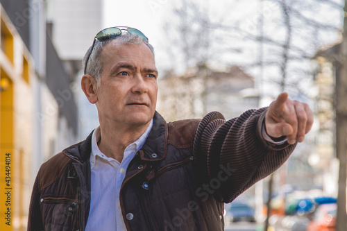Elegant mature man walking on an urban sidewalk and pointing a direction © tetxu