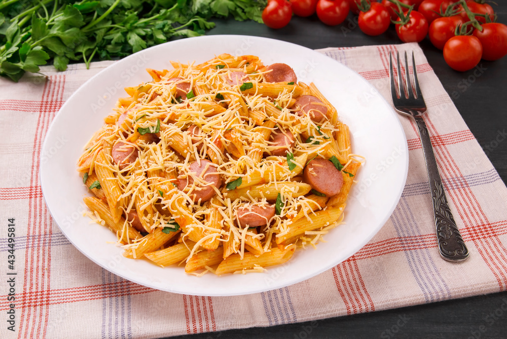 Penne pasta in tomato sauce with sausages and cheese, decorated with parsley on a black background Penne pasta in tomato sauce with sausages and cheese, decorated with parsley on a black background