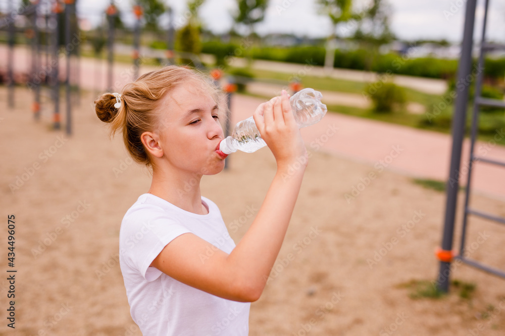 Portrait of a teenage girl drinking water from a bottle on a sports field
