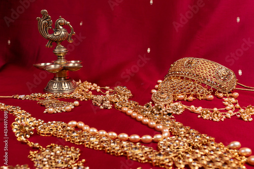 Indian traditional bronze oil lamp in the shape of a bird and gold Indian female jewelry on the red saree background. traditional Indian religious ceremony of Hindus. Diwali