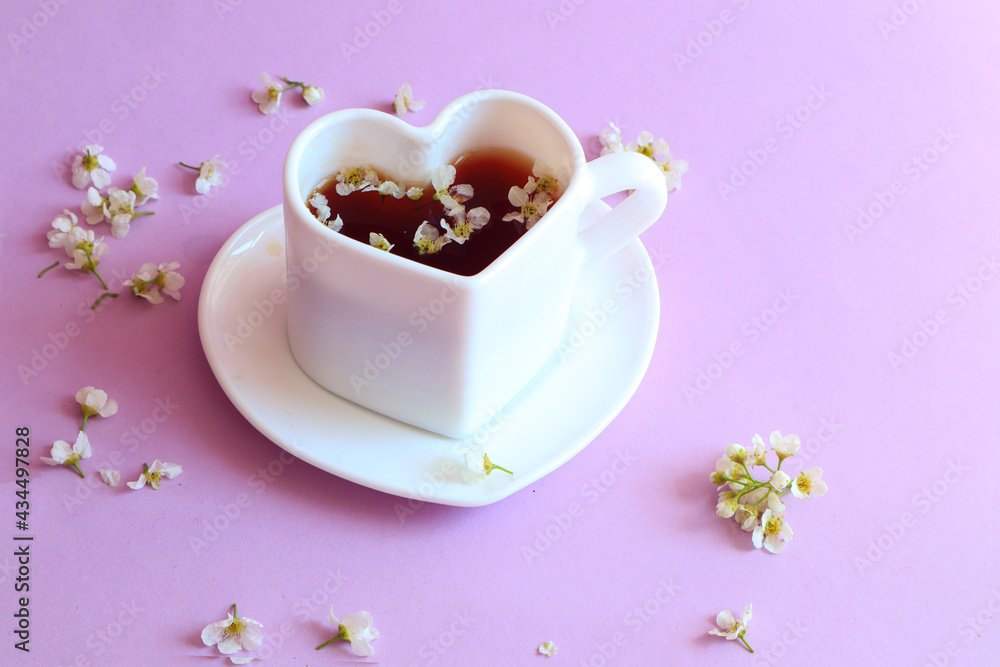 A cup of tea in the form of a heart with scattered petals of white delicate flowers on a pastel background, side view, space for text A cup of tea in the form of a heart with scattered petals of white delicate flowers on a pastel background, side view, space for text