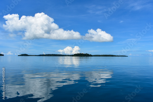 Reflection of the cloud on the sea. Clouds and sea in the tropical waters. The horizon line between the sea and the blue sky with cloud. An island as the horizon line. Seascape.