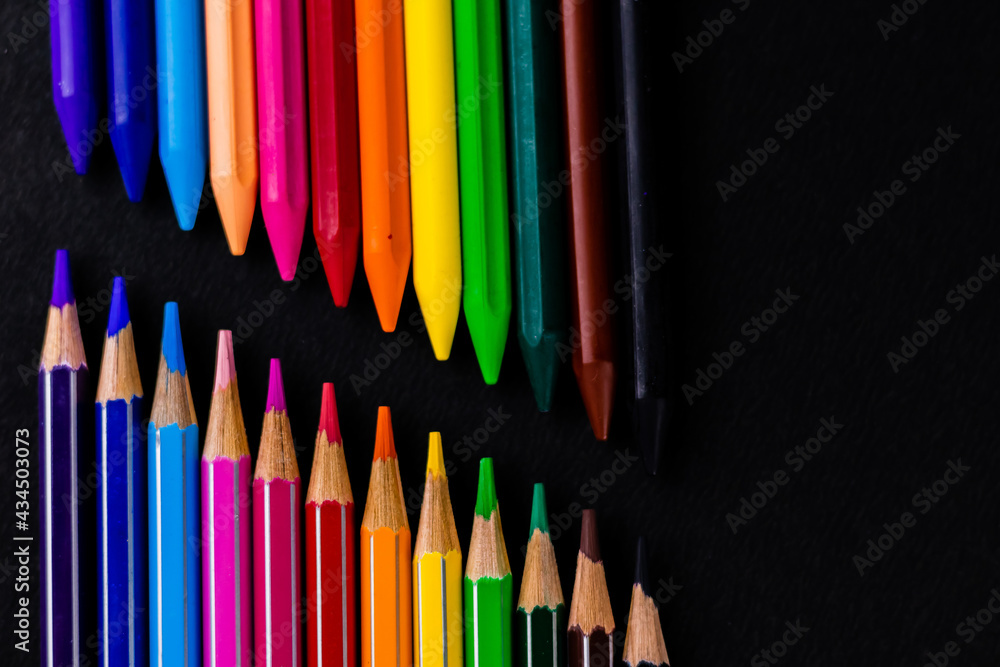 Wax crayons and color pencils arranged on black background with their nibs facing each other -Fine Arts concept. Wax crayons and color pencils arranged on black background with their nibs facing each other -Fine Arts concept.