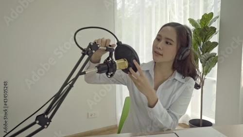 Beautiful asian young woman radio host working, setting microphone, preparing to speak before recording podcast and live on social media. Technology of on-air online in broadcasting at home studio.