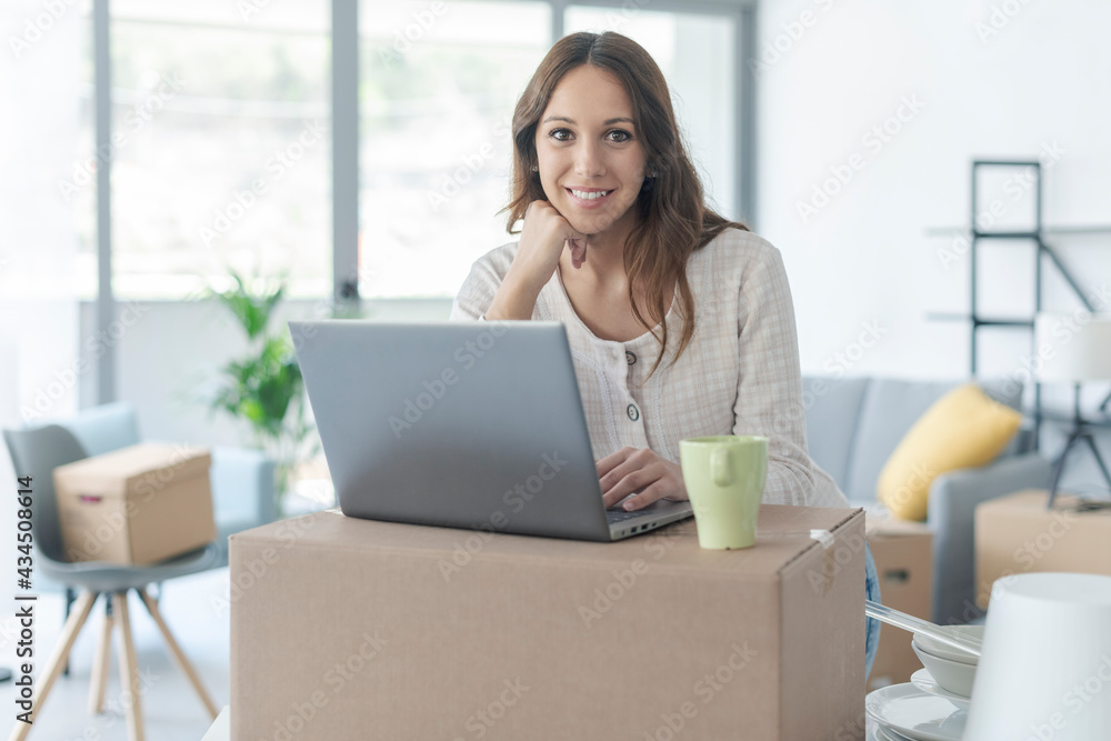 Happy woman moving in her new house and using her laptop Happy woman moving in her new house and using her laptop