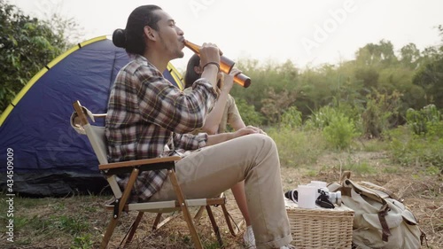 Enjoy asian young woman, girl and man cheering with beer bottle, sitting on chair . Adventure couple, people camping in forest. Eco activity, lifestyle nature on holiday concept.