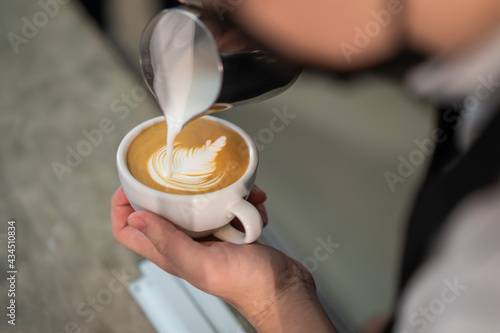 Close-up shot of barista pouring milk on coffee to make latte art.