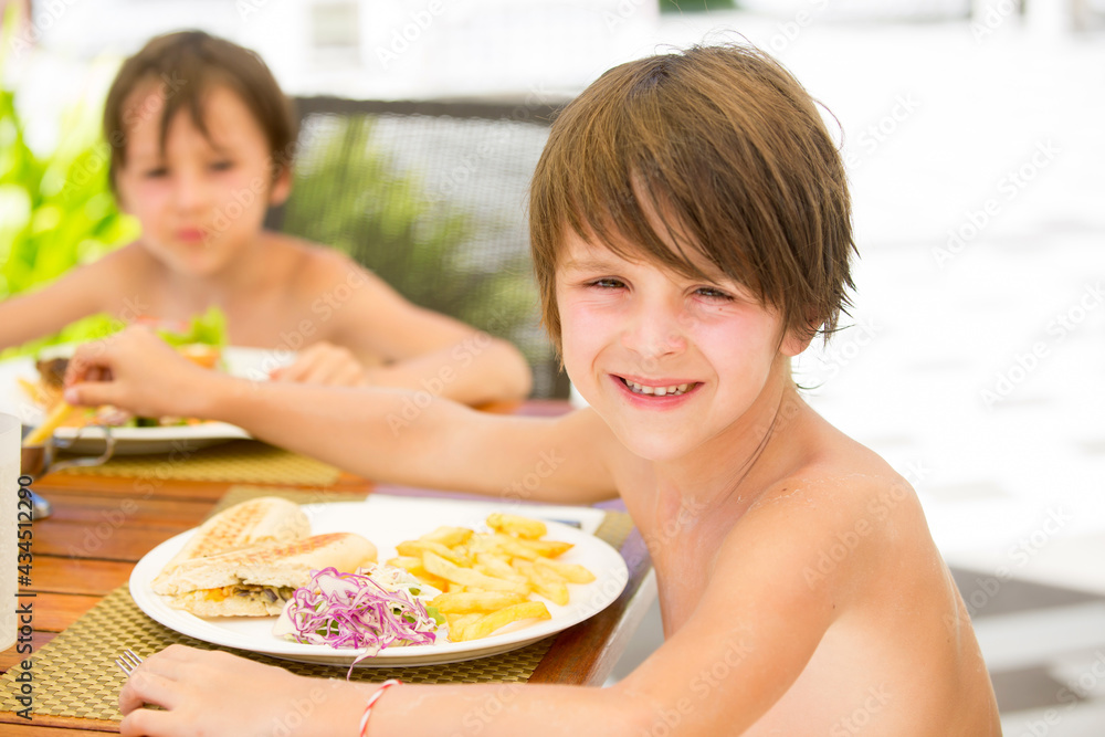 Sweet preschool boy, eating fresh hamburger in a restaurant on beach summer resort Sweet preschool boy, eating fresh hamburger in a restaurant on beach summer resort