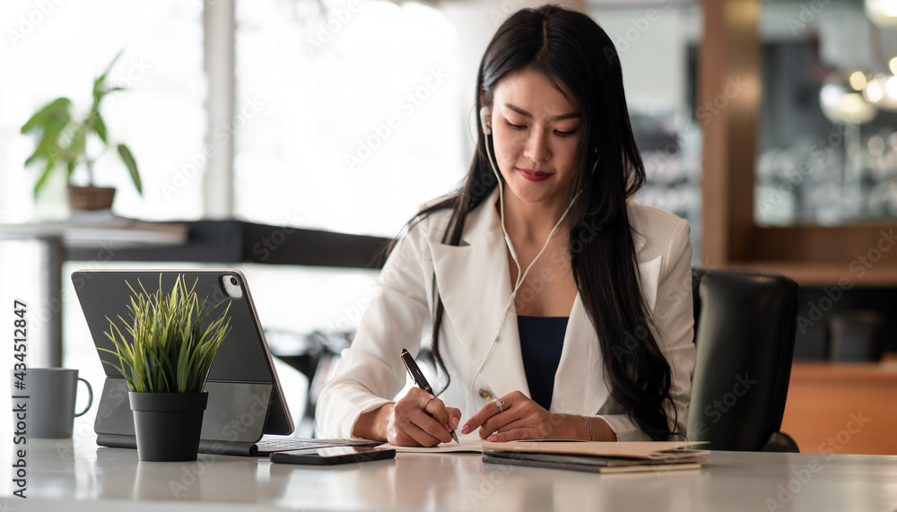 Businesswoman with earbuds for video conference lecture note.woman using tablet webinar video course at home office Businesswoman with earbuds for video conference lecture note.woman using tablet webinar video course at home office