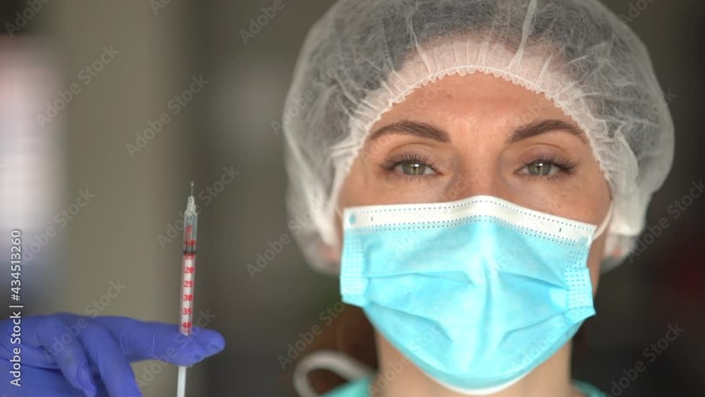 Woman holding syringe with dose of covid-19 vaccine. Portrait of a nurse wearing a mask and a protective cap and glasses Woman holding syringe with dose of covid-19 vaccine. Portrait of a nurse wearing a mask and a protective cap and glasses