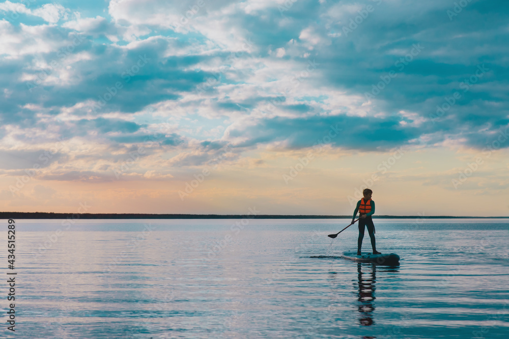 Kid riding on paddle sup surfboard in water at sunset