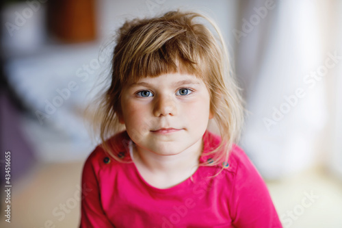Portrait of happy smiling toddler girl indoors. Little preschool child with blond hairs looking at the camera.