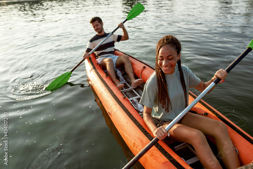 Excited young couple enjoying paddling kayak on a river together on a summer afternoon