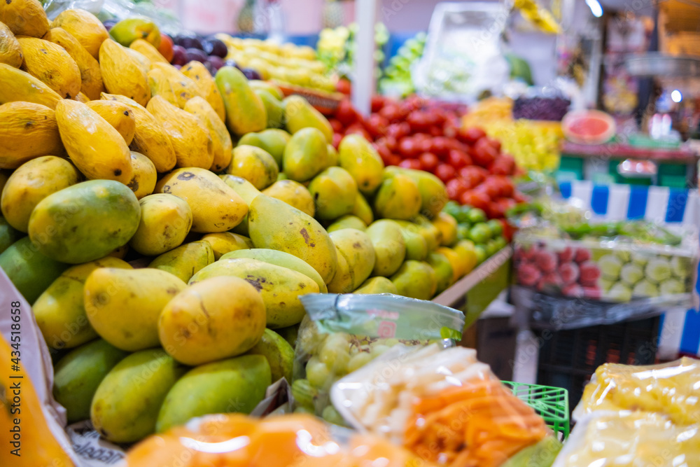 Colorful fruit stand with green and yellow mangoes, and more