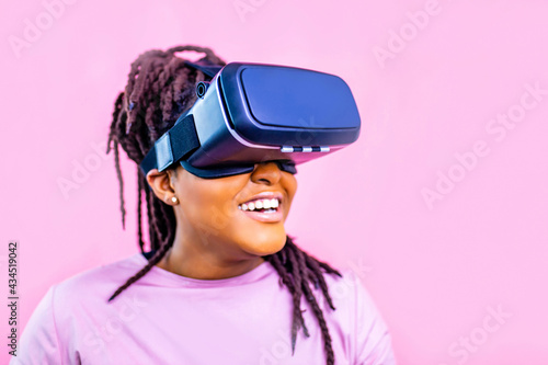 black ethnic woman watching video life simulation in studio pink background © yurakrasil