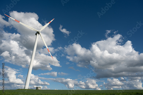 Windrad in grüner Landschaft vor blauem Himmel mit strahlend weißen Wolken