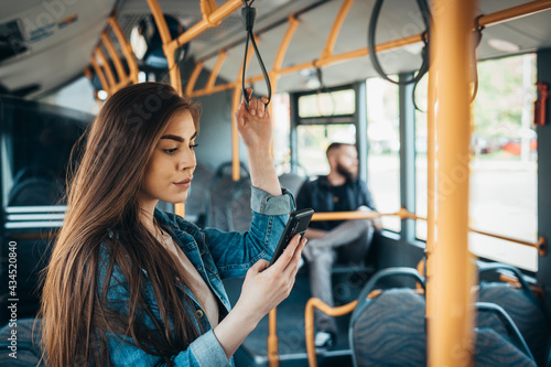 Woman using a samrtphone while standing in a moving bus photo