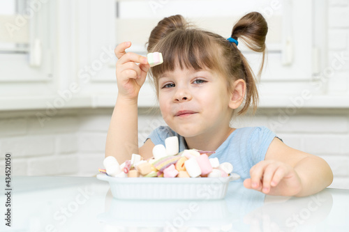 kid girl sitting at the kitchen table and eating marshmallows