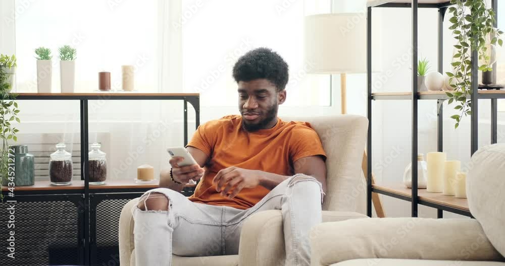 Young man using mobile phone while relaxing on armchair at home Young man using mobile phone while relaxing on armchair at home