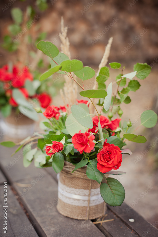 Decorations in rustic style: beautiful bouquets from red roses in a flowerspot decorated by sackcloth