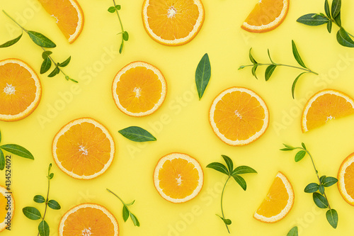 Summer bright background with oranges and green leaves on the yellow surface