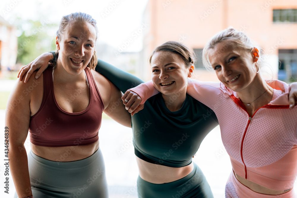 portrait of three sporty women of different shape hugging each other and smiling to camera