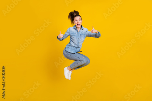 Full length body size photo young pretty girl jumping up showing thumb up gesture isolated vivid yellow color background