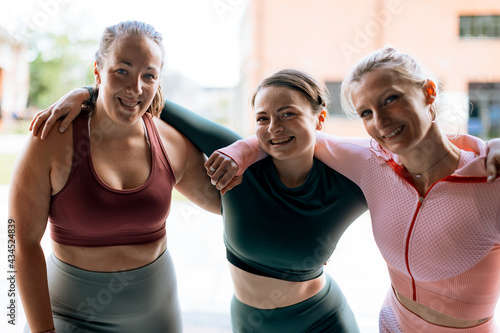 portrait of three sporty women of different shape hugging each other and smiling to camera