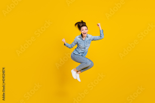 Full length body size photo young pretty girl jumping up gesturing like winner isolated bright yellow color background