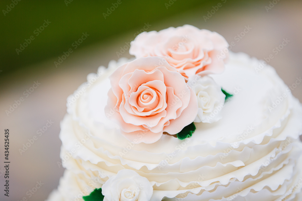 Beautiful big wedding cake with three storey decorated by tender sweet roses. Outdoor. a white wedding cake with three levels and red roses Beautiful big wedding cake with three storey decorated by tender sweet roses. Outdoor. a white wedding cake with three levels and red roses