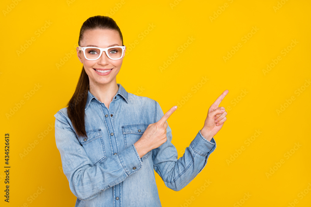 Photo of sweet adorable young lady dressed jeans shirt spectacles pointing fingers empty space smiling isolated yellow color background Photo of sweet adorable young lady dressed jeans shirt spectacles pointing fingers empty space smiling isolated yellow color background