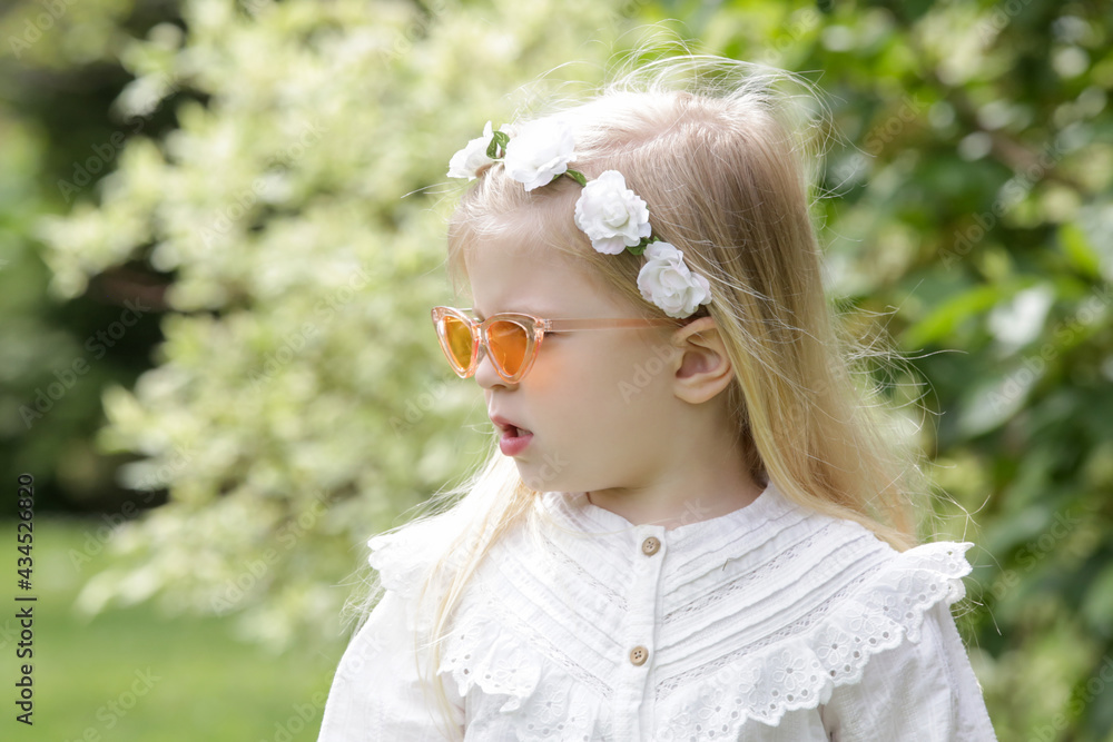 Portrait of fashionable toddler girl with long blonde hair in retro white shirt and sunglasses on a sunny summer day in park. Portrait of fashionable toddler girl with long blonde hair in retro white shirt and sunglasses on a sunny summer day in park.