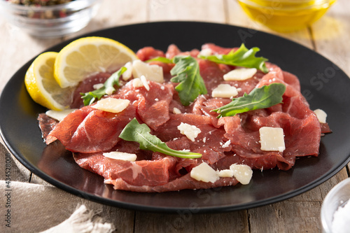 Marbled beef carpaccio on black plate on rustic wooden table