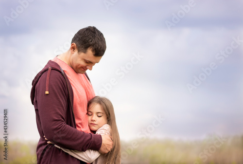 Daughter with closed eyes hugs dad tightly outdoors in summer. Soft focus in fog. Overcast