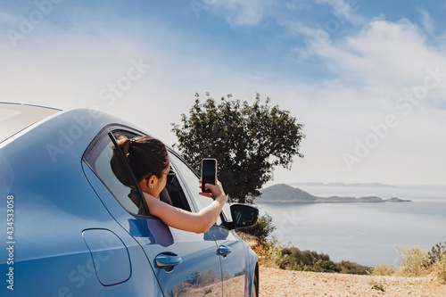 Photography Young woman taking picture with smarphone from open window of a car