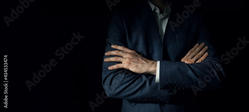 businessman in suit with crossed arms standing on dark black background. copy space photo