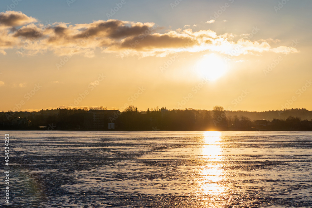 Winter landscape with frozen lake at sunrise or sunset. Lake glistening ice reflect a sun.Forest in the background. Winter landscape with frozen lake at sunrise or sunset. Lake glistening ice reflect a sun.Forest in the background.