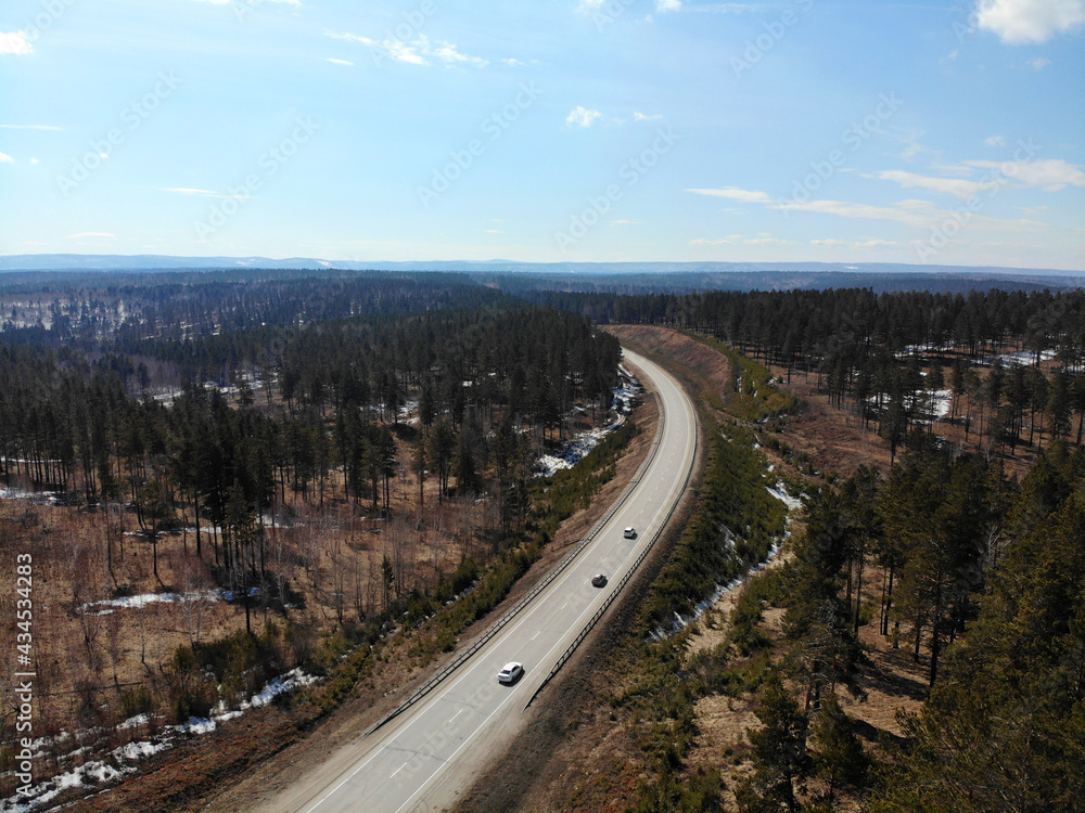 Cars drive on an asphalt road through a spring forest. Aerial view. 