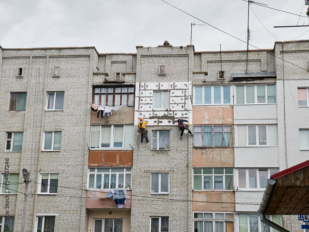 Two workers insulate a typical Soviet house. Energy saving concept.